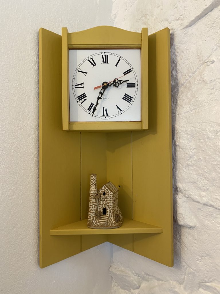 A cute yellow old fashioned clock with a small ornament of a cornish mine