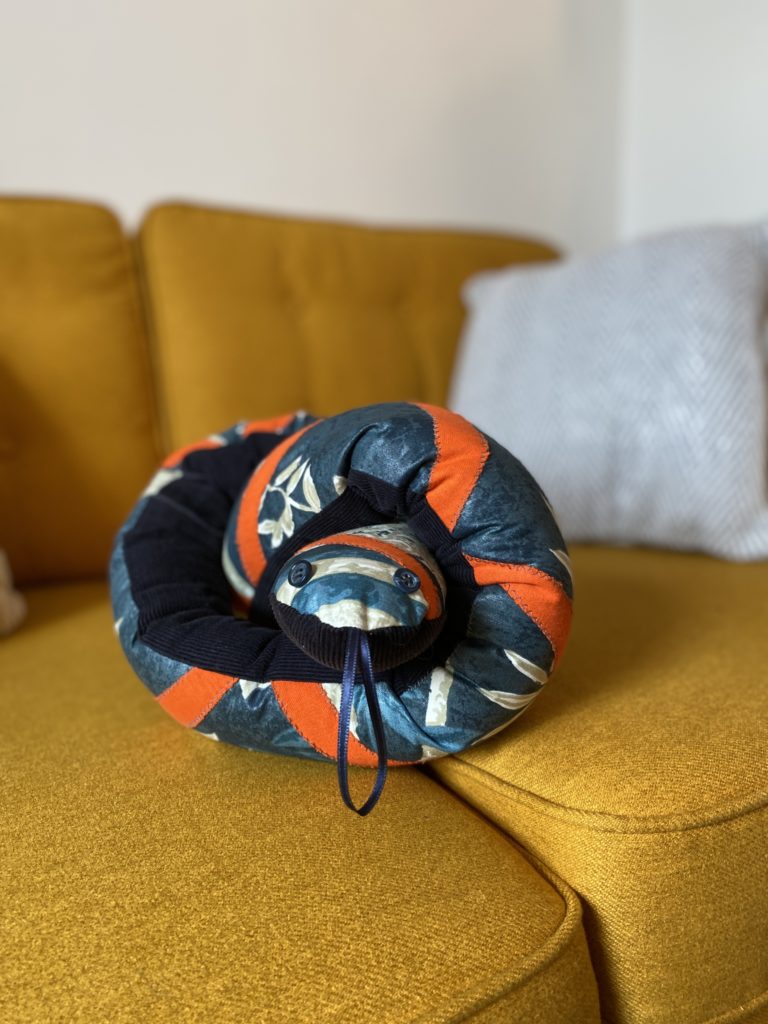 A handmade draught excluder that looks like a snake on a yellow sofa
