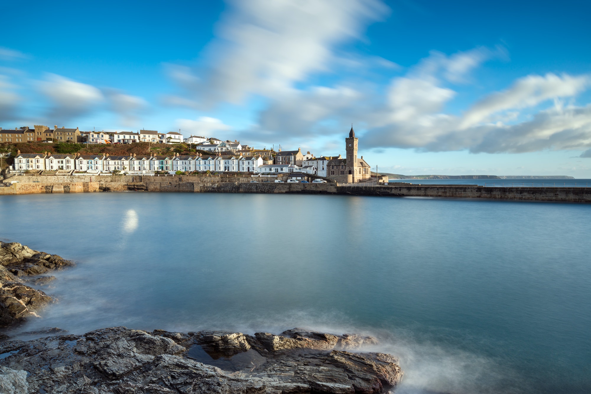 Porthleven harbour with calm water in the foreground and the houses painted white next to the church